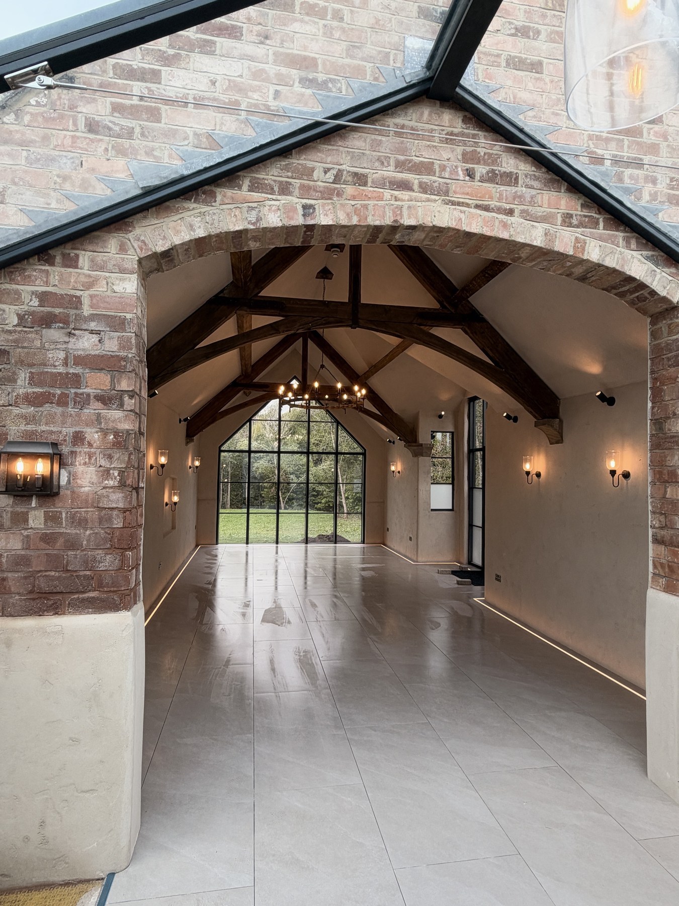 Rebuilt barn interior with a large tiled floor, exposed timber roof beams and a brick archway